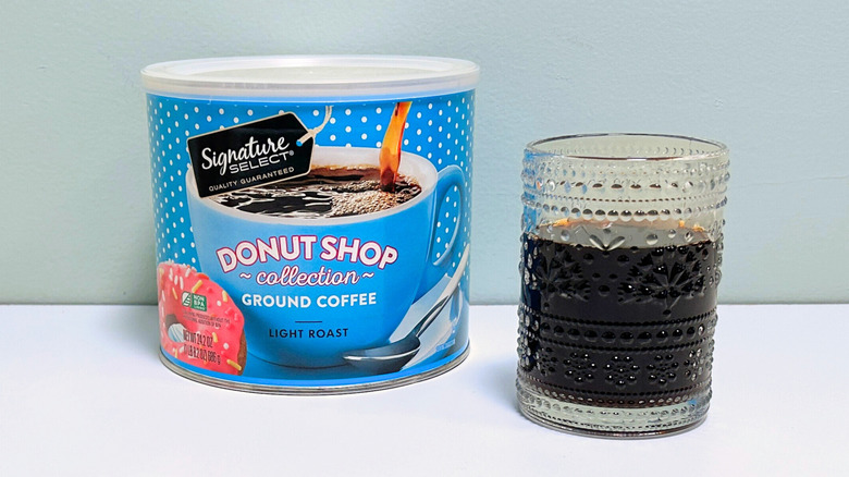 A glass cup filled with coffee next to a can of Signature Select Donut Shop Collection Ground Coffee