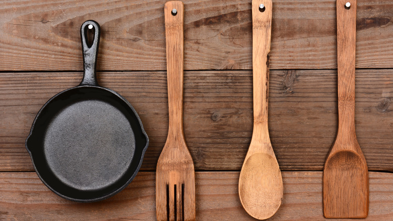 A cast iron frying pan and three wooden utensils hanging on a wooden wall