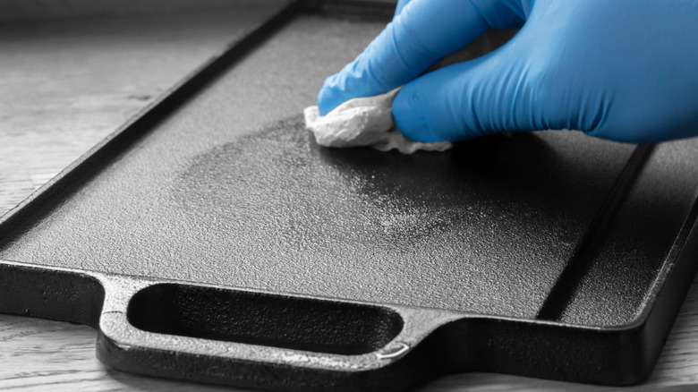 A person wipes a cast iron griddle with oil
