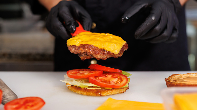 A fast food worker in black gloves assembling a cheeseburger