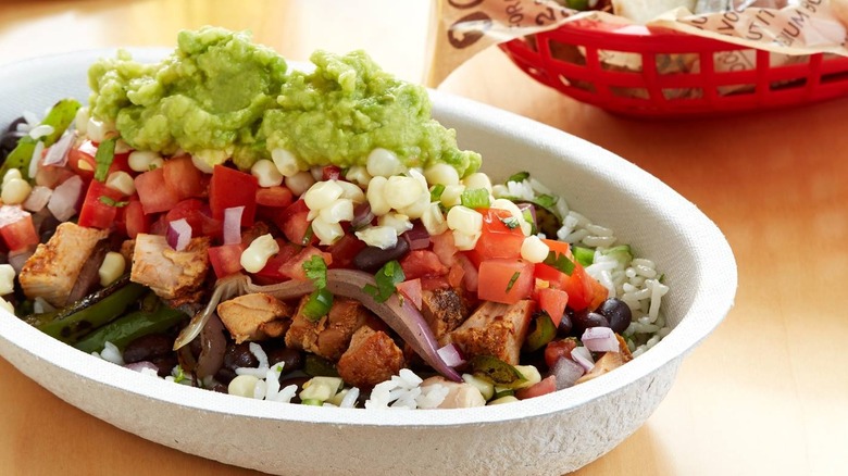 A Chipotle burrito bowl with corn, guacamole, beans, chicken, and rice