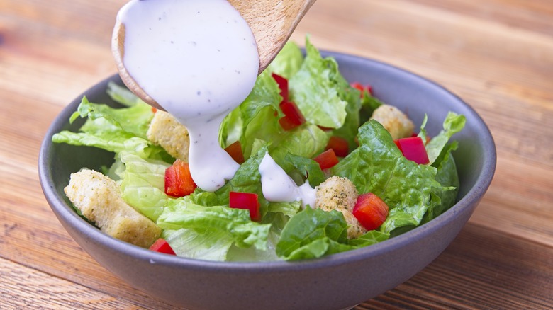 Ranch dressing being poured from a spoon onto a salad