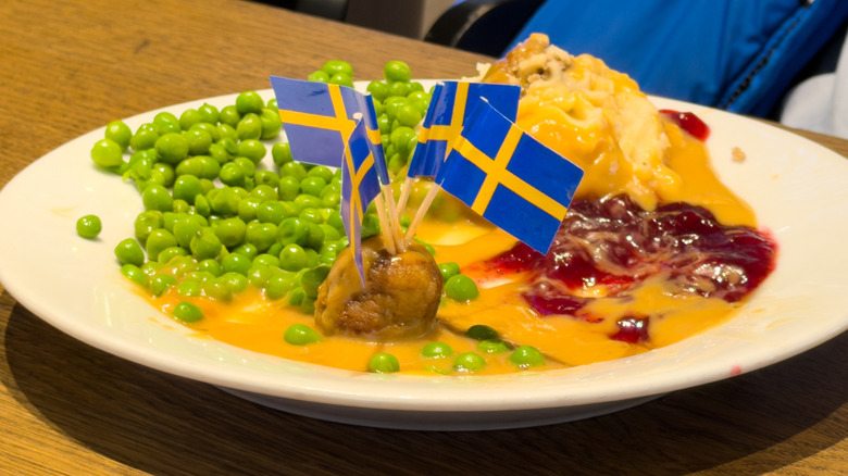 A plate of IKEA meatballs with sides, with multiple mini Swedish flags stuck in one meatball