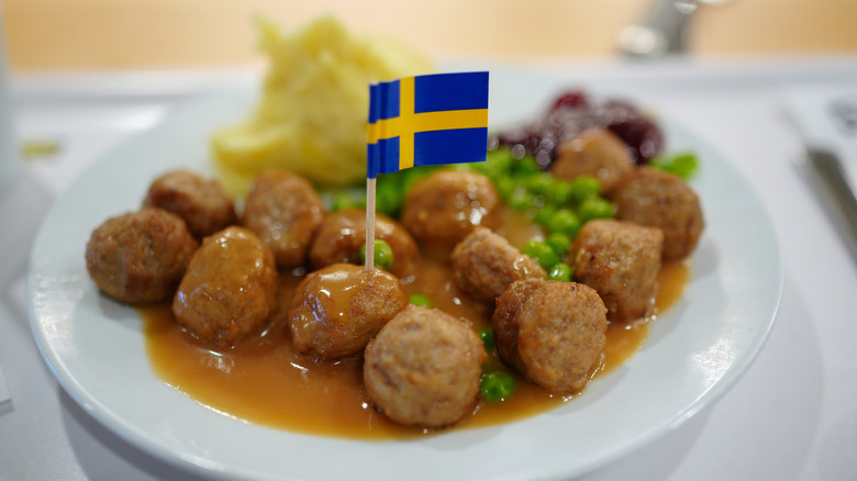 A plate of IKEA meatballs, peas, mashed potatoes, and lingonberry jam, with a miniature Swedish flag stuck into one of the meatballs
