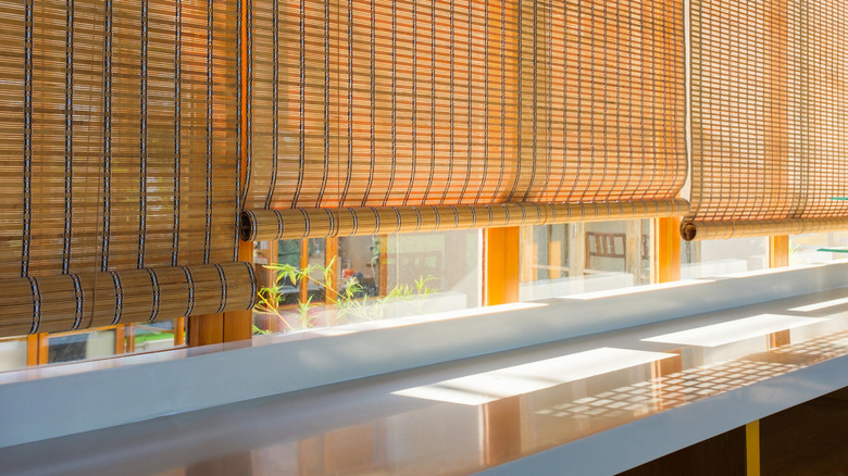 Rolling bamboo curtains hanging over a large, bright window