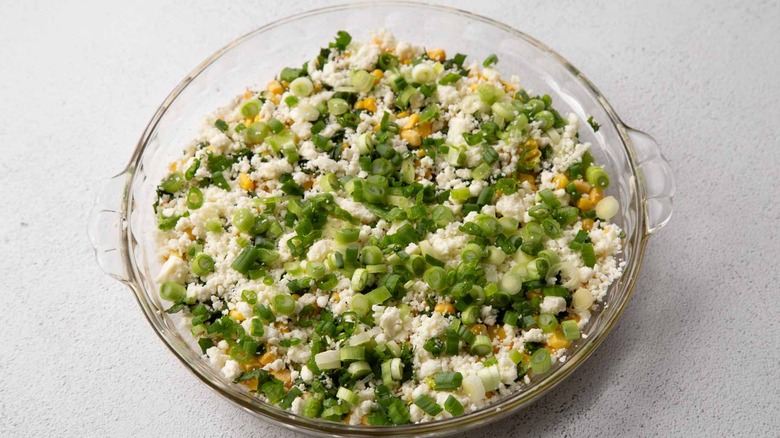 crumbly white cheese and green onions in a clear pie plate