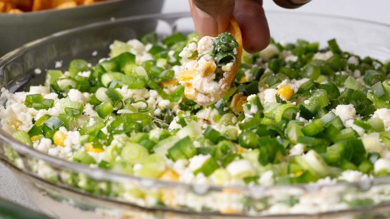 hand dipping a tortilla chip into crumbly white cheese, green onions, and corn