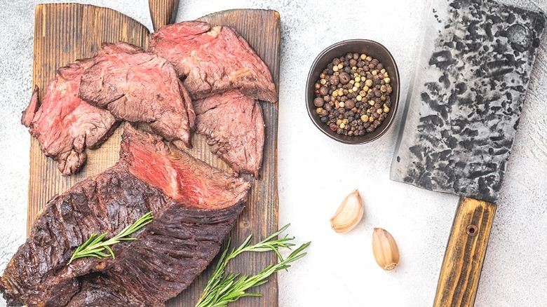 Cooked hanger steak diaphragm beef cut sliced with juicy medium doneness, herbs garlic and spices on a board.