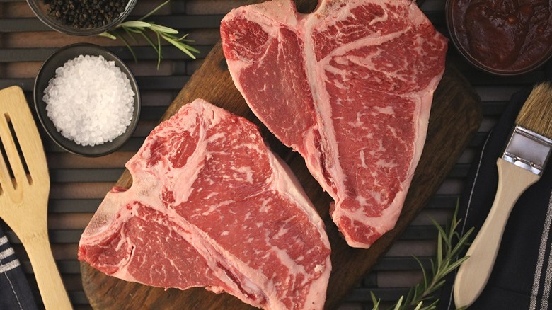 Two porterhouse steaks, uncooked, with a ramekin of salt flakes and a wooden spoon
