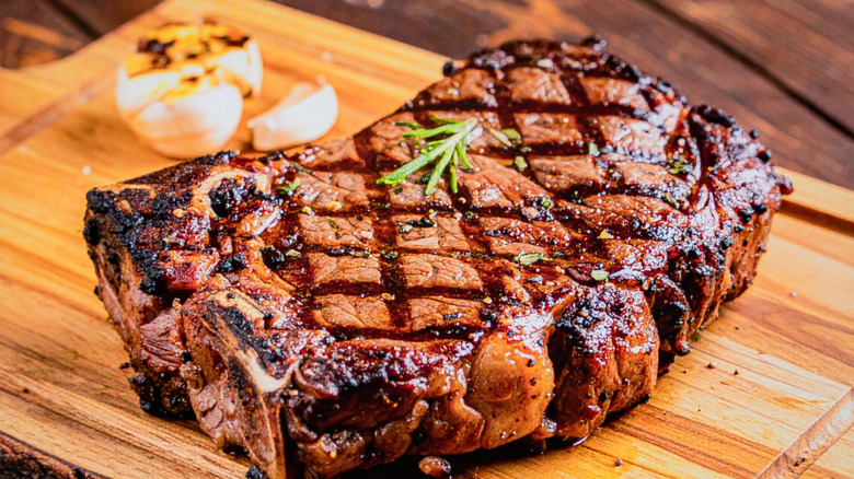 Grilled Ribeye Steak, seared with herbs and garlic, on a wooden board