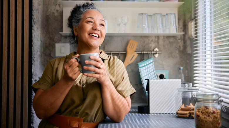 Woman holding mug in kitchen with generic coffee maker in the background