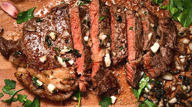 seared medium rare sirloin steak on the chopping board basted in butter, garlic, shallot and parsley