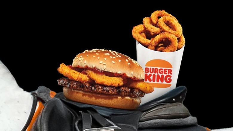 A Rodeo Burger and a container of onion rings on a saddle on the back of a white horse