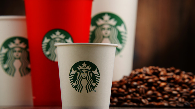 White and red Starbucks cups and a big pile of coffee beans