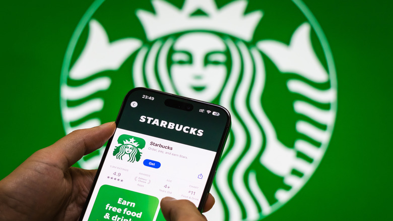 Starbucks app on iPhone in front of a green Starbucks sign