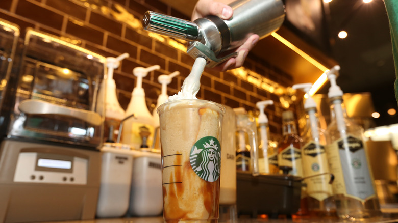 Strbucks barista pouring whipped cream onto a venti coffee