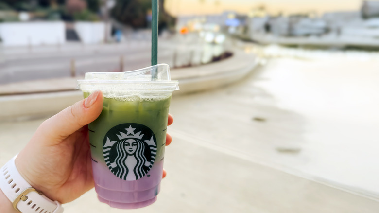 Hand holding a purple and green Starbucks drink with a green straw