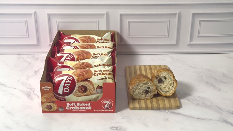 Box of 7 Days chocolate croissants and one cut in half on a wooden cutting. board