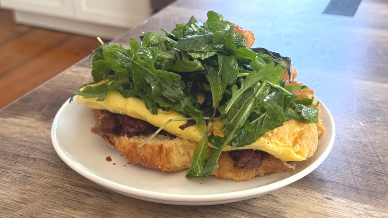 Homemade croissant sandwich with egg, bacon, cheese, and arugula