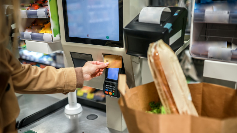 Person paying for a bag of groceries and a baguette