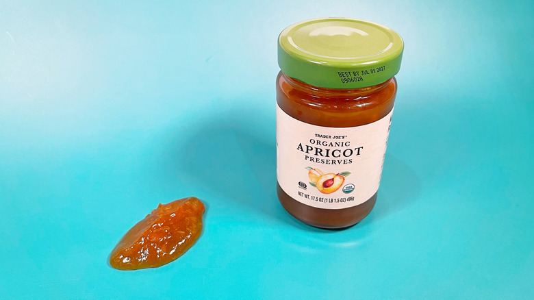 Trader Joe's apricot preserves with a spoonful next to the jar on a blue background