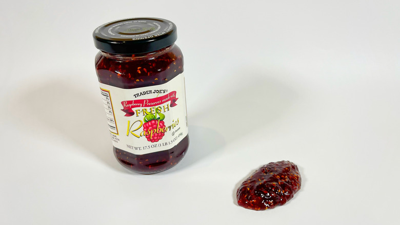 A jar of Trader Joe's raspberry preserves next to a spoonful on a white background