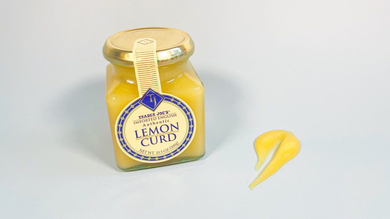 A jar of Trader Joe's lemon curd on a white background next to a spoonful of the curd