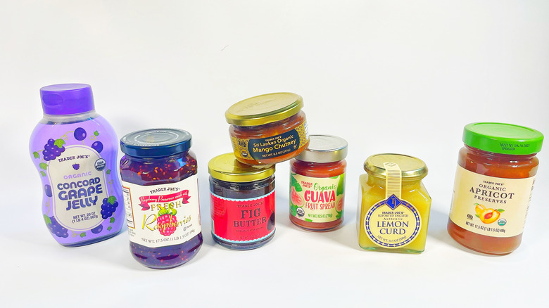 Seven containers of Trader Joe's jams, jellies, and fruit spreads on a white background
