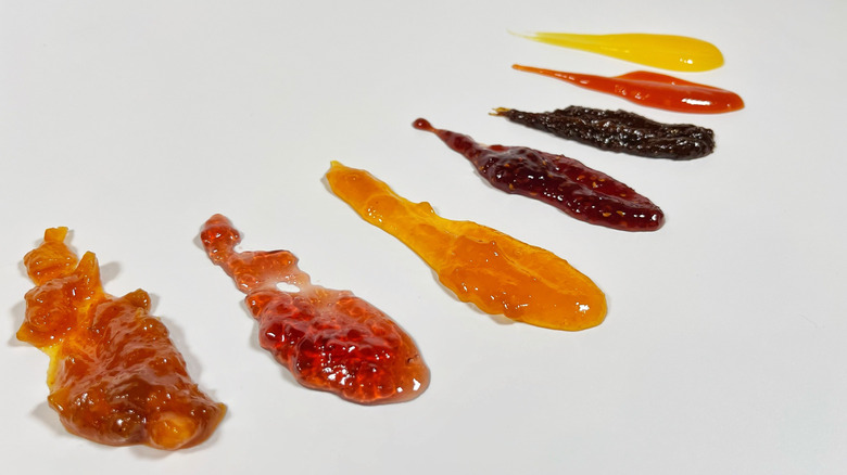 Seven spoonfuls of different jams and jellies on a white background
