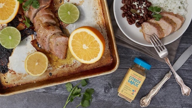 Citrusy garlic seasoning bottle next to sheet pan and bowl with dinner on a white plate