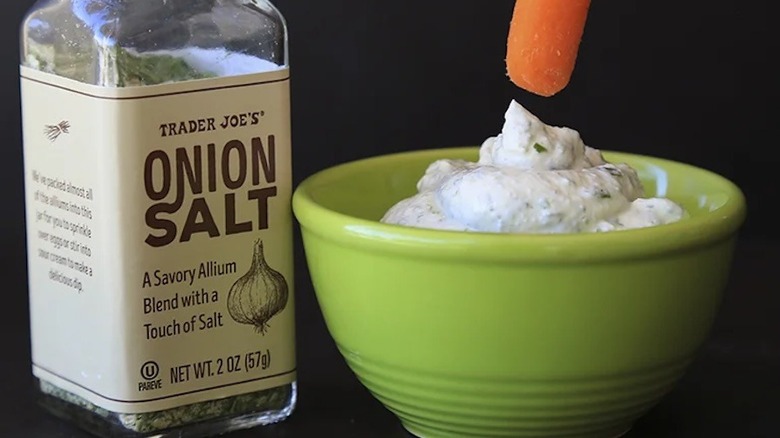 Onion salt bottle next to dip in a green bowl with a carrot going toward it