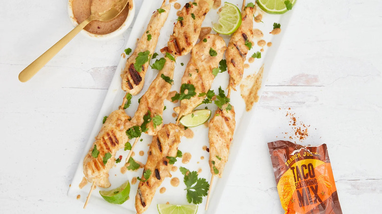 Taco seasoning mix next to grilled chicken skewers with a white background