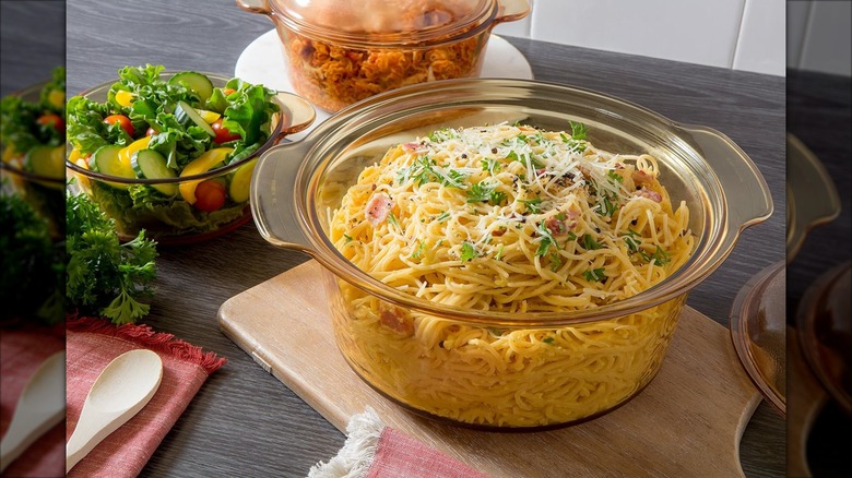 Glass Dutch oven full of pasta with smaller glass cookware with food