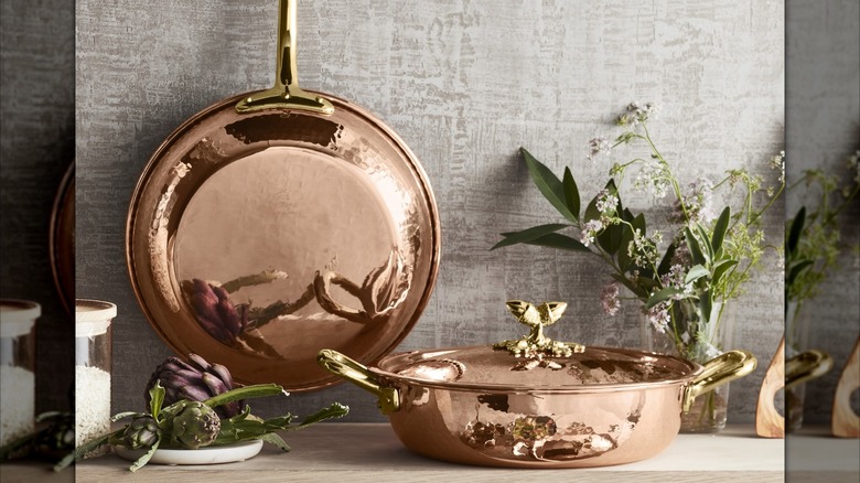 Ruffoni Historia hammered copper pans with decorative acorn-handled lids on counter with greenery