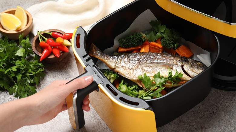 Yellow air fryer drawer filled with vegetables and a full fish
