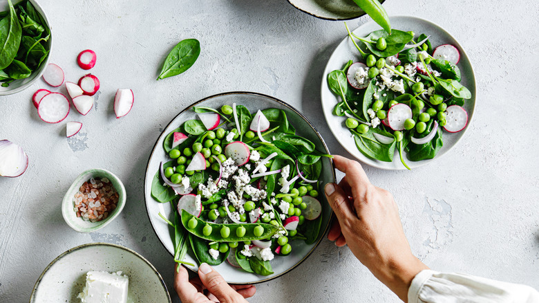 Two white bowls of spinach salad with radishes, fresh peas, and cheese