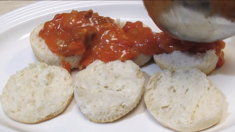 three biscuits sliced in half, with a ladle drizzling red tomato gravy over the top