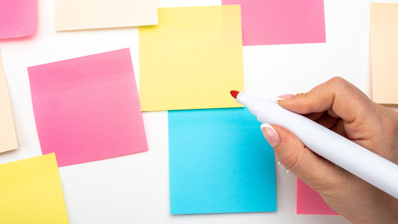 Hand holds marker over colorful scattered Post-it Notes