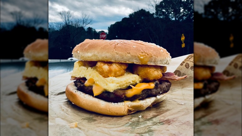 A Burger King breakfast sandwich on a burger bun with hashbrowns, outside, underneath a stormy sky