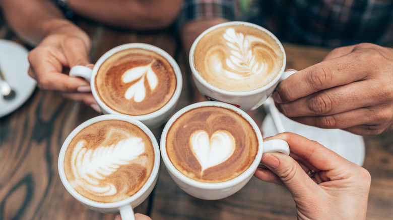 Friends holding coffee mugs with latte art up in a cheers