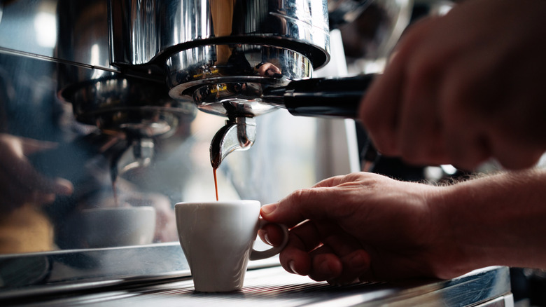 Hand pouring an espresso shot into white expresso mug
