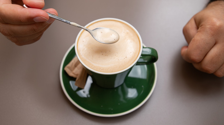 Spoon dipped into microfoam milk from a latte in a green mug
