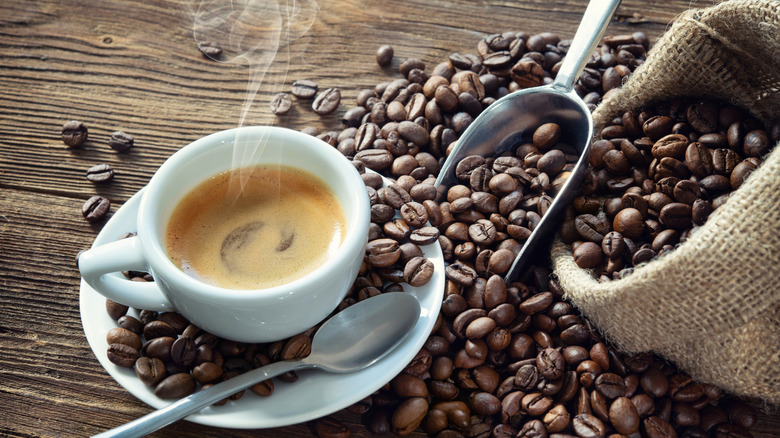 Steaming espresso mug surrounded by spilled coffee beans
