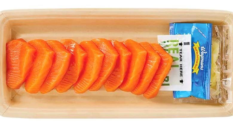 A tray of salmon sashini with packets of sauces on the side