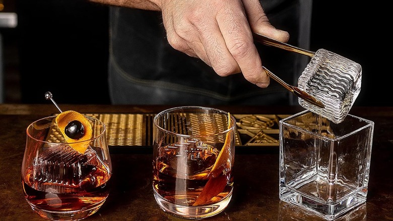 Three rocks glasses with decorated ice, hand puts ice in one glass
