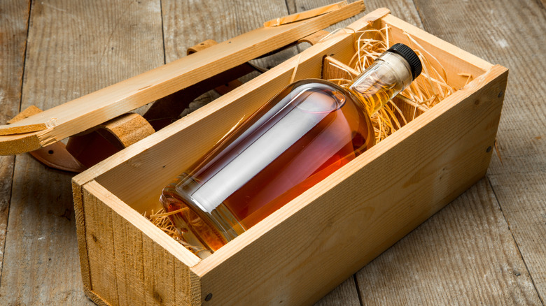 Bottle of brown liquor in a wood box with straw