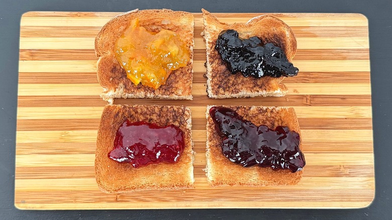 Pieces of toast on a cutting board with different jellies and spreads