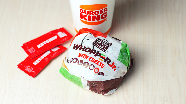 A wrapped Whopper Jr with cheese at Burger King, with ketchup packets and a drink