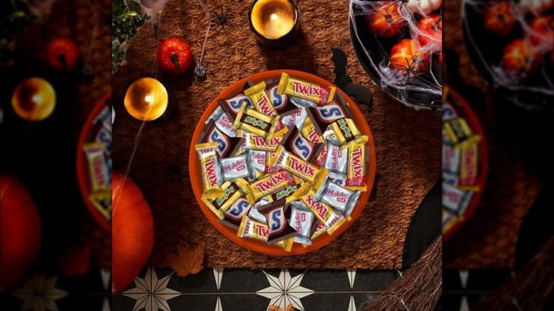 A bowl of fun size Snickers, Twix, Milky Way, and Three Musketeers on a Halloween table