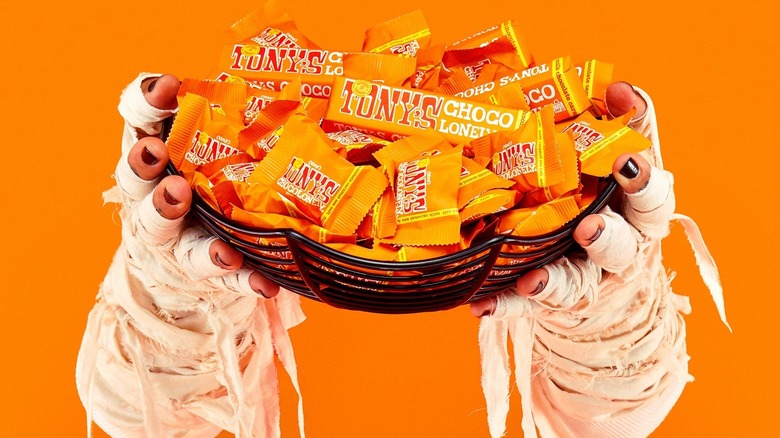 Mummy hands hold up a spiderweb bowl of mini and small Tony's Chocolonely bars